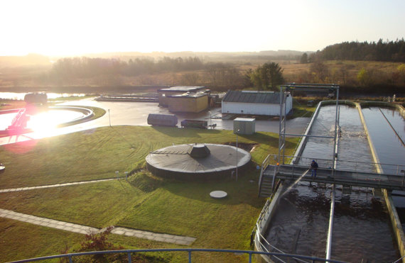 Wastewater treatment facility with settling tanks and surrounding landscape at sunrise.