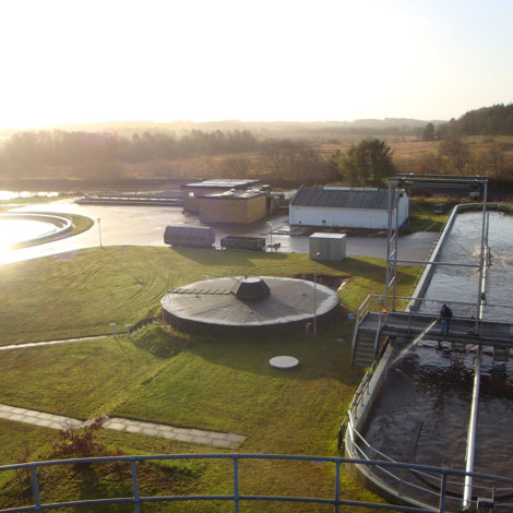 Wastewater treatment facility with settling tanks and surrounding landscape at sunrise.