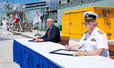 海军军官和官员在HMCS Harry DeWolf舰附近签署文件。